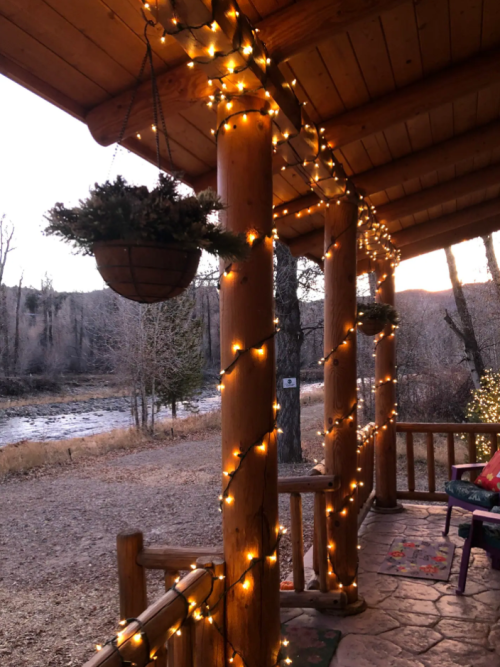 A cozy porch decorated with string lights, overlooking a serene river and trees at dusk.